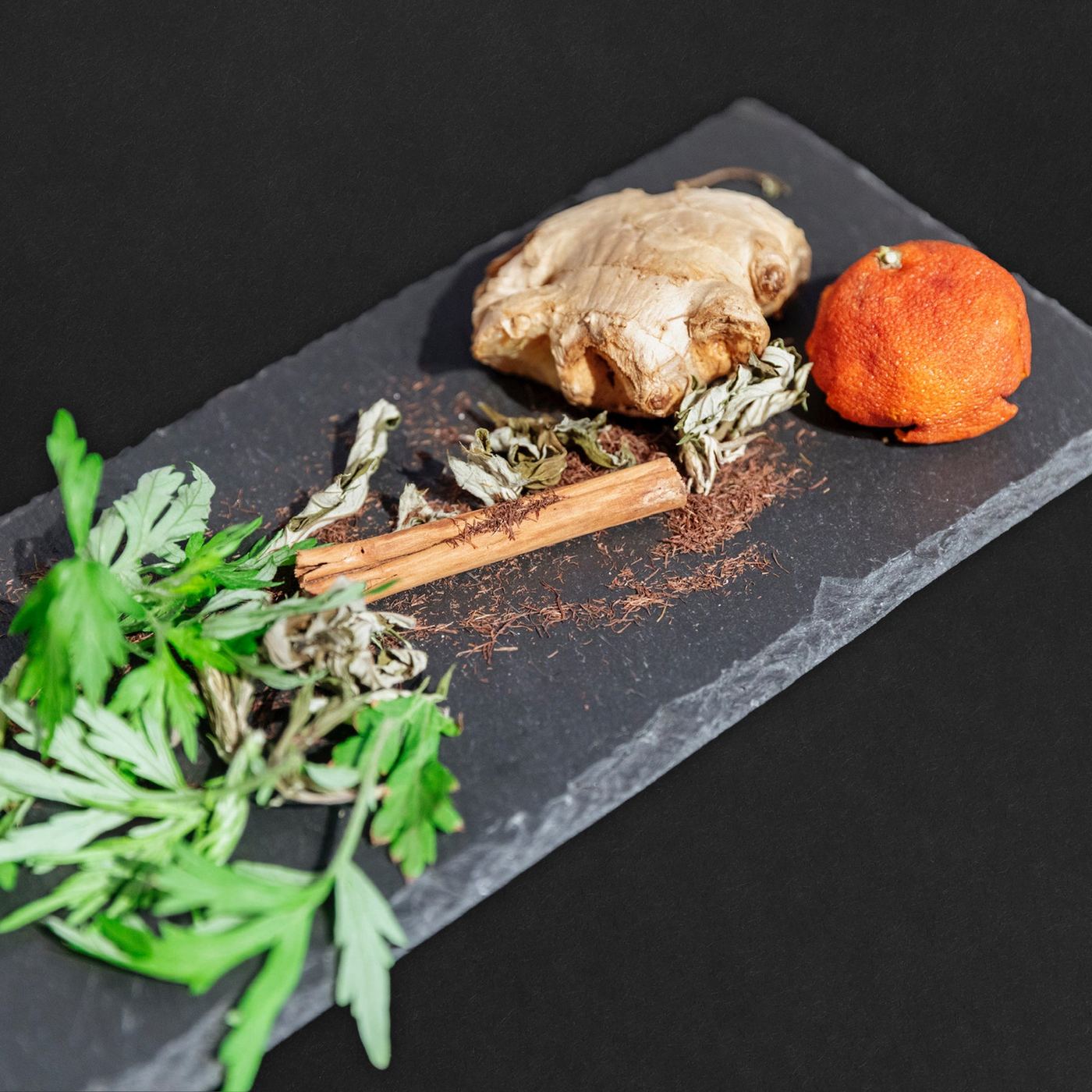 Mugwort, ginger, a cinnamon stick and dried citrus on slate