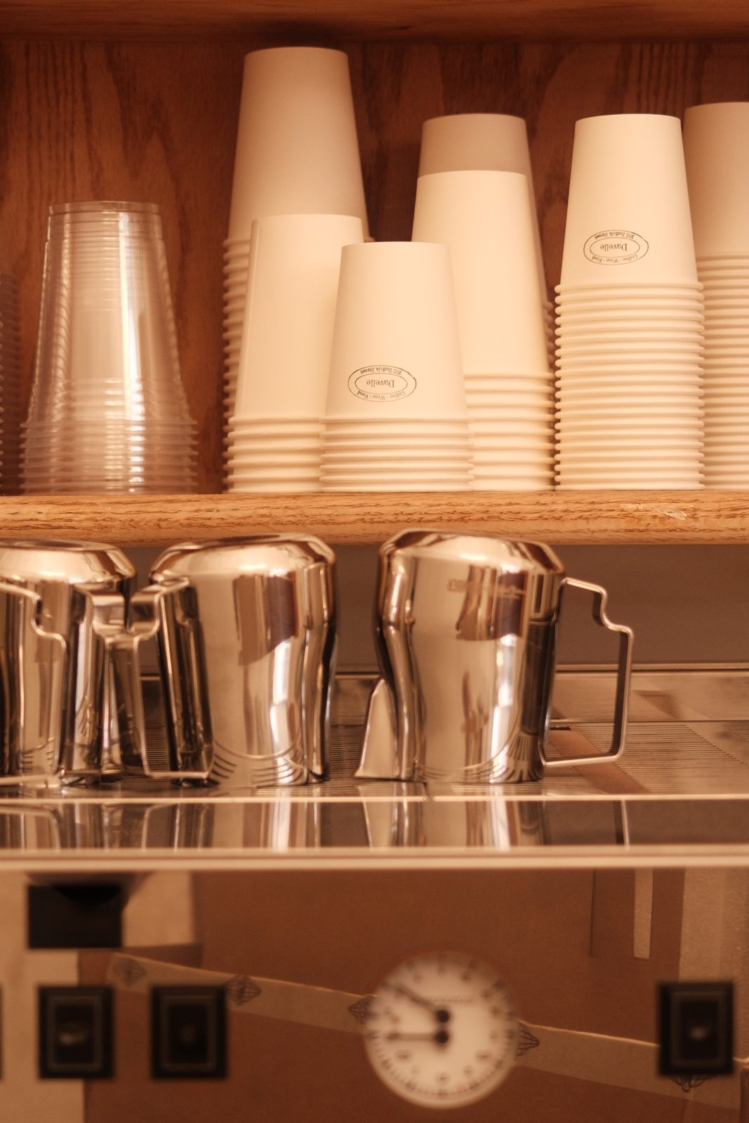 Paper cups and steel pitchers above the espresso machine