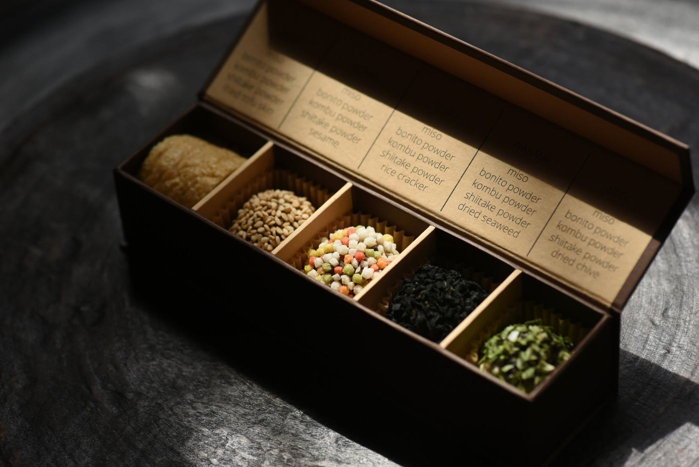 An open MISOMARU box with five hand-rolled miso balls, on dark weathered wood