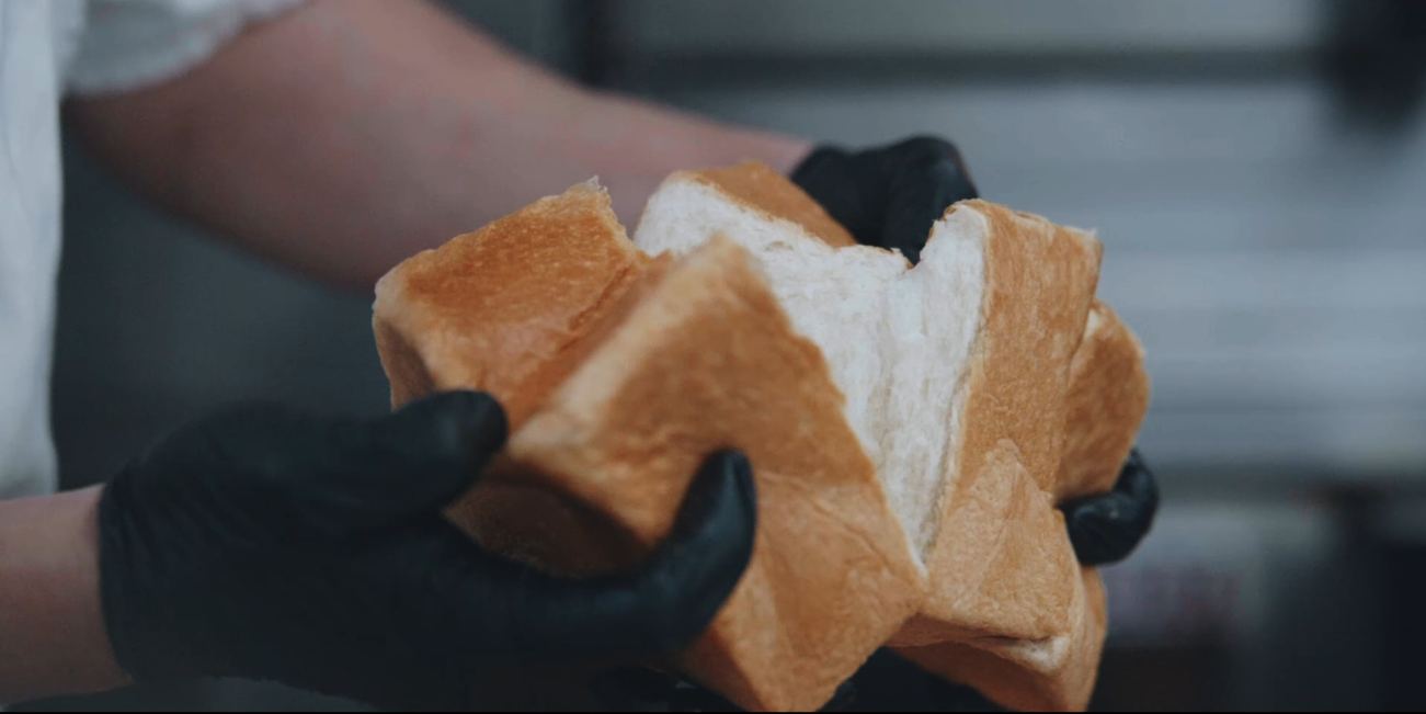 Gloved hands pulling a shokupan loaf apart to show the white crumb